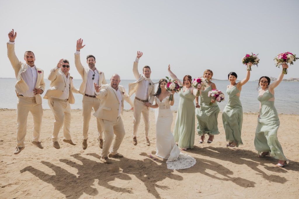 International couple with bridesmaids and groomsmen jumping on the beach – Getting married in Alicante